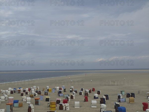 Colourful beach chairs spread out on the wide, sandy beach under a cloudy sky with a view of the