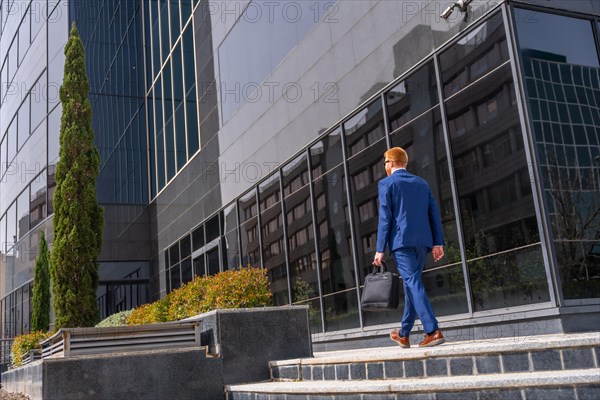 Full length rear view of a businessman with laptop bag and suit walking along a financial district