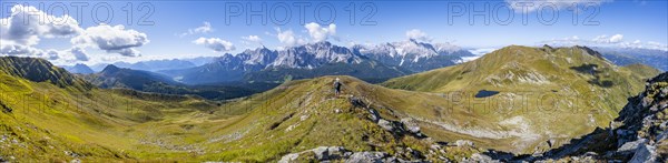 Panorama, mountaineer on a hiking trail between green mountain meadows on a mountain ridge,