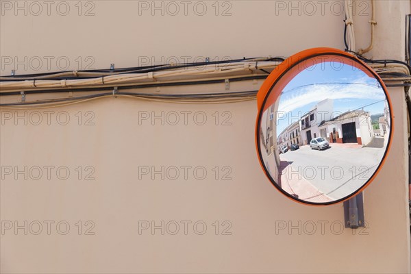 A traffic mirror on the facade of a building reflects a street in the
