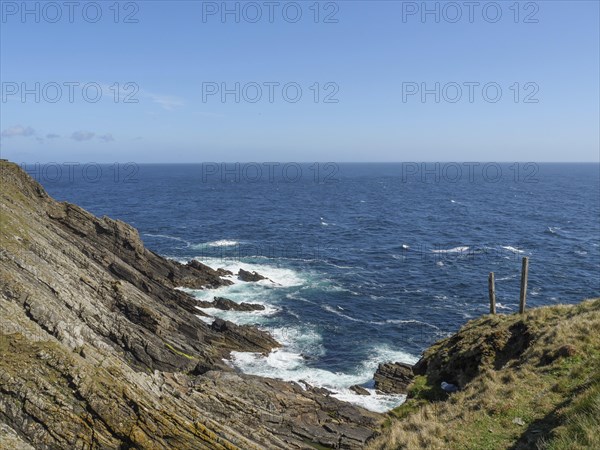 View of a rocky coastline with green grass and blue sea under a clear sky, green meadows on a deep