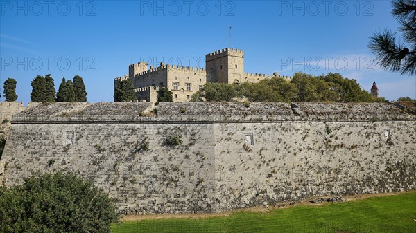 View of a castle across a large stone fortress wall, against a blue sky, Grand Master's Palace,