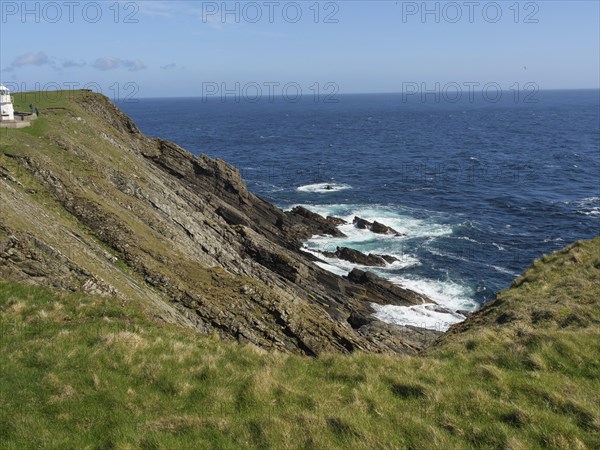 Steep cliffs with green grass and views of the azure sea and undulating coastline under a blue sky,