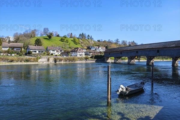 View of a calm river with a boat, a bridge and houses along the shore, embedded in a green hilly