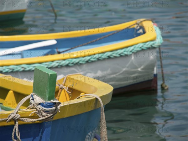 Close-up of a part of a yellow and blue fishing boat in the water, many colourful fishing boats in