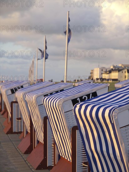 Row of striped beach chairs at sunset by the sea, with buildings and clouds in the background, blue