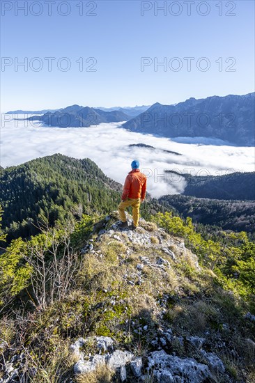 Mountaineer on the rocky summit of the Ettaler Manndl, view over mountain landscape and sea of