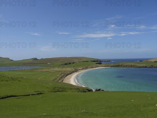 A breathtaking coastal landscape with an elongated beach surrounded by green meadows and clear blue
