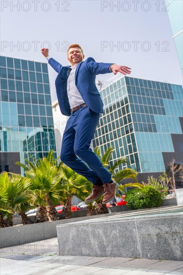 Vertical photo of a happy businessman jumping next to financial building