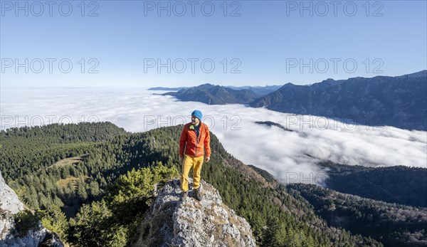 Mountaineer on the rocky summit of the Ettaler Manndl, view over mountain landscape and sea of