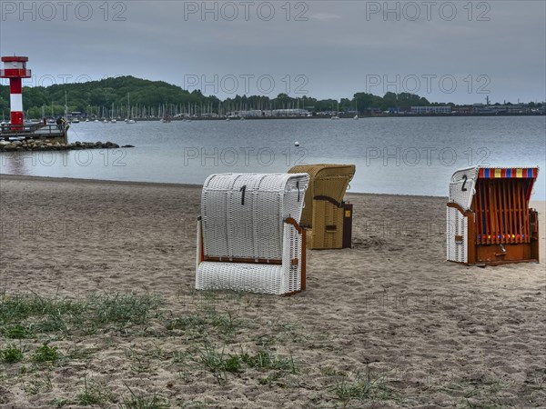 A cloudy day on the beach with a lighthouse in the background and several beach chairs on the sand,
