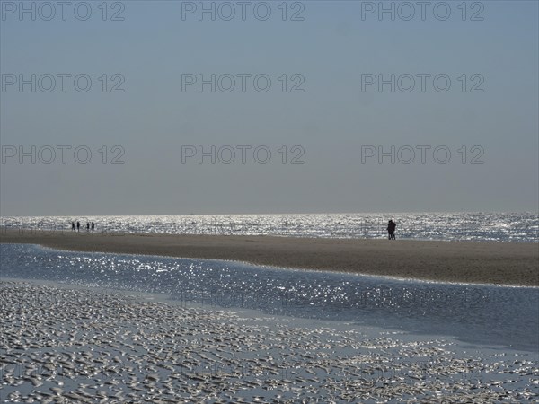 People walking along the beach with reflecting watercourse, glittering sea water at low tide on the