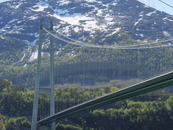 Bridge against a backdrop of snow-capped mountains and green forests under a clear blue sky, bridge