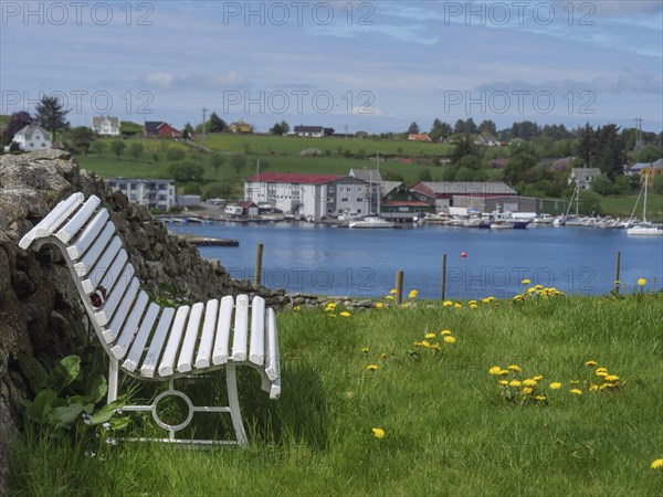 White bench on a green meadow with a view of the sea, yachts and a small village in the background,