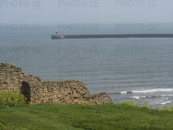 A piece of coastline with ruinous architecture in the foreground and the sea in the background,