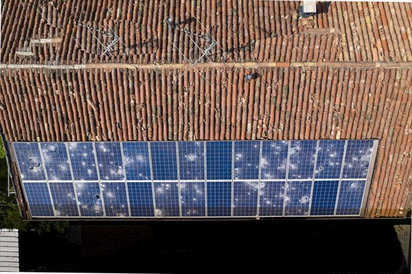Direct overhead view of a roof with terracotta tiles and damaged solar panels casting shadows