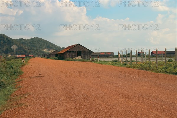 A serene rural landscape with a dirt road leading past wooden salt storage houses and mountains in