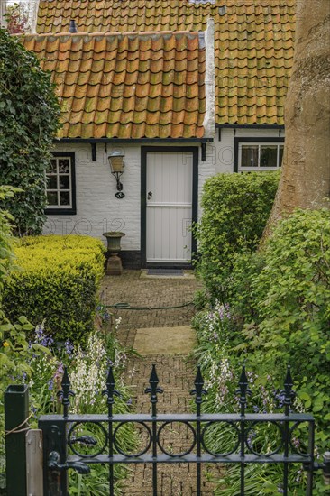 Small cosy house with red tiled roof and well-kept garden, old houses with green gardens in a small