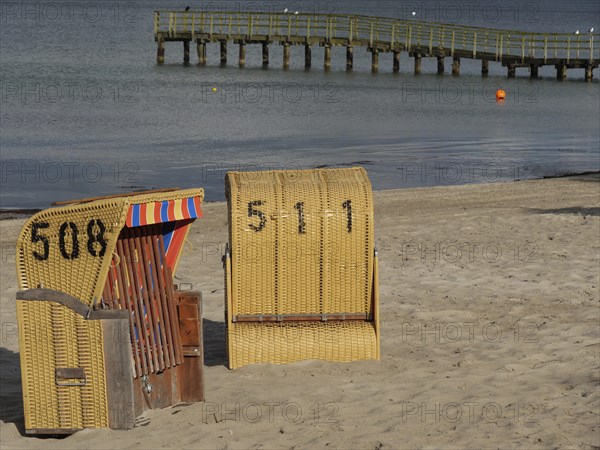 Two beach chairs on the beach near a wooden jetty with calm sea in the background, beach chairs on