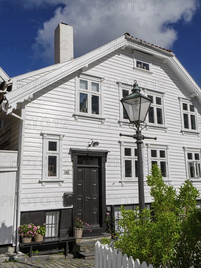 White houses with black doors, flowers and lanterns along a cobblestone street under a blue sky,