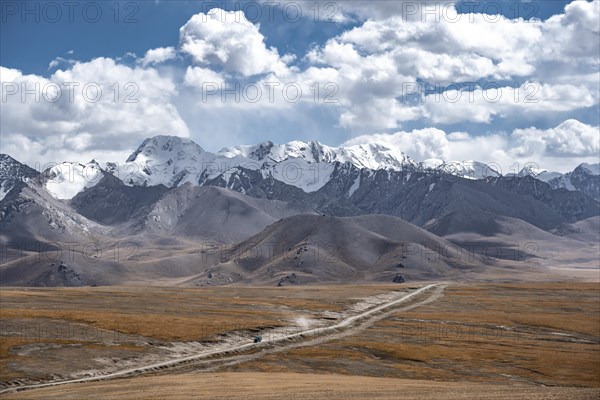 Car on a gravel track in the high mountain plateau, glaciated and snow-covered peaks, Ak Shyrak