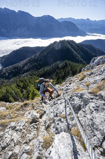Hiker on via ferrata to Ettaler Manndl, view over mountain landscape and sea of clouds, high fog in