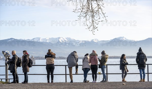 People enjoying the view of snow-covered mountain peaks on Lake Constance in winter, Lindau Island,