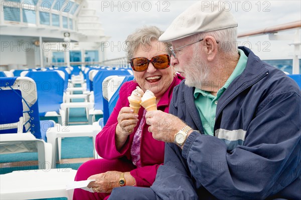 Happy senior adult couple enjoying ice cream on the deck of a luxury passenger cruise ship