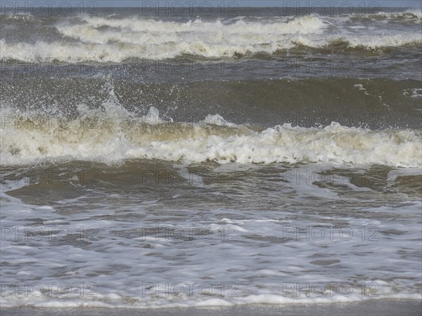 Close-up of churning waves and splashing water in the sea, waves on a beach, sunny day with clouds