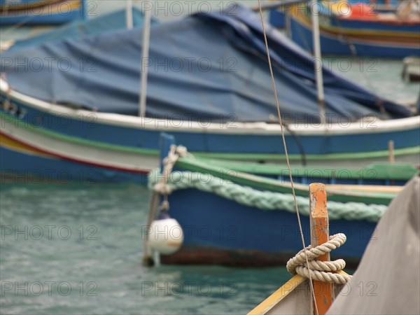 Several boats are quietly moored in the clear waters of a harbour, many colourful fishing boats in