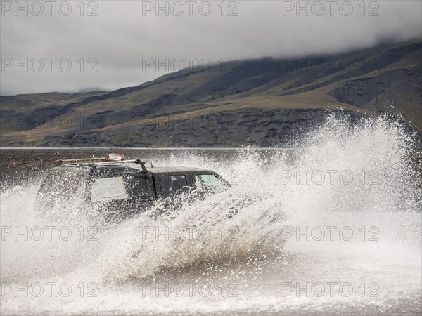 An off-road vehicle quickly crosses a waterway and causes large water fountains in front of a