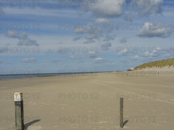 Wide, quiet sandy beach with posts in the foreground under a cloudy sky, clouds on the beach with