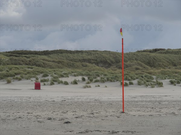 A lonely flagpole stands on a sandy beach in front of a hilly dune landscape, colourful beach