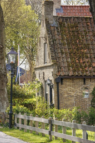 Historic house with tiled roof, fence and street lamp, surrounded by trees in spring, historic