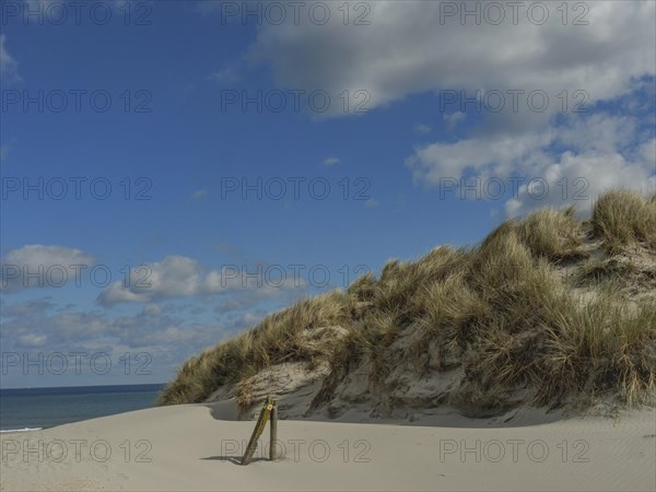 High sand dunes with grass, behind them the sea and a partly cloudy sky, dunes on an island with a