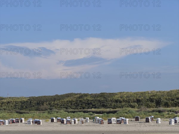 Beach with many beach chairs in front of large dunes, impressive cloud formation in the sky, dunes