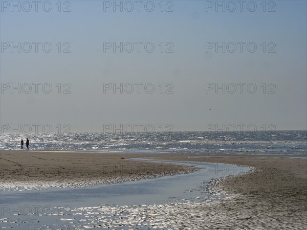 People walking along the beach with a watercourse under a clear blue sky, sparkling sea water at