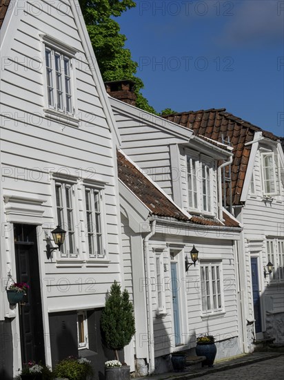 Narrow alley with white wooden houses with red tiled roofs and flowering plants, white wooden