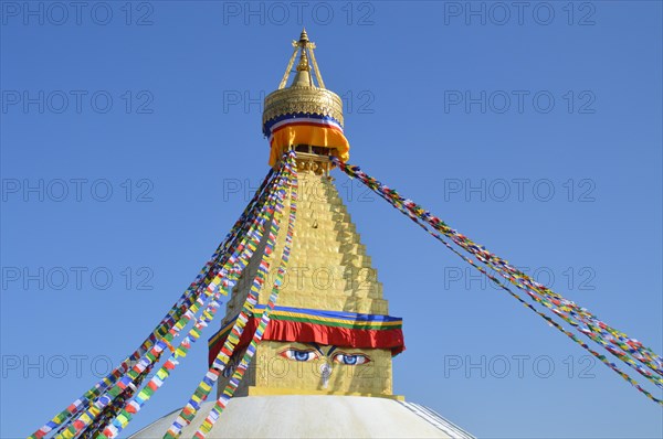 Top part of Boudhanath Stupa or Chaitya adorned with colorful prayer flags under a clear blue sky
