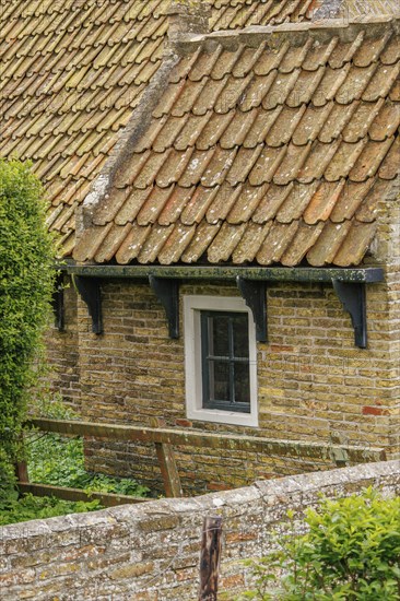 Small brick house with rustic tiled roof and surrounded by fresh green bushes, old houses with