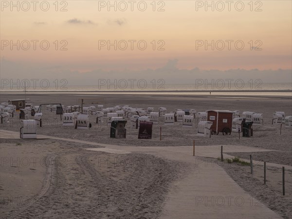 A quiet beach with white beach chairs and a peaceful orange sunset on the horizon, setting sun on a