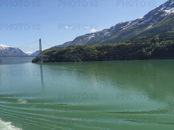 View of a bridge over a calm lake, surrounded by snow-capped mountains and dense forests, bridge in