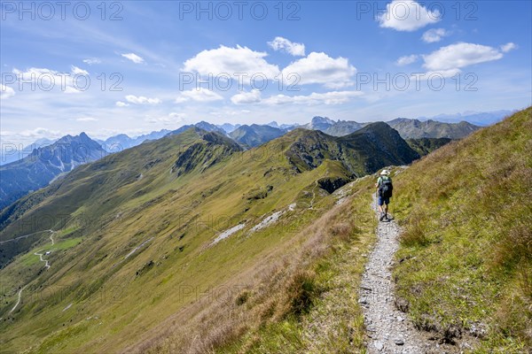 Mountaineer on a hiking trail on a grassy mountain ridge, idyllic mountain landscape with green