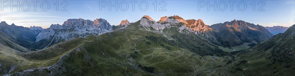 Alpine club hut, mountain landscape with green mountain meadows and rocky peaks at sunrise,