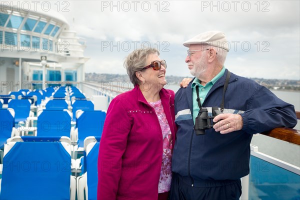 Senior adult couple enjoying the view from their passenger cruise ship with their bonoculars