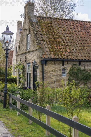 Small brick house with tiled roof and garden, surrounded by fresh spring greenery, rustic