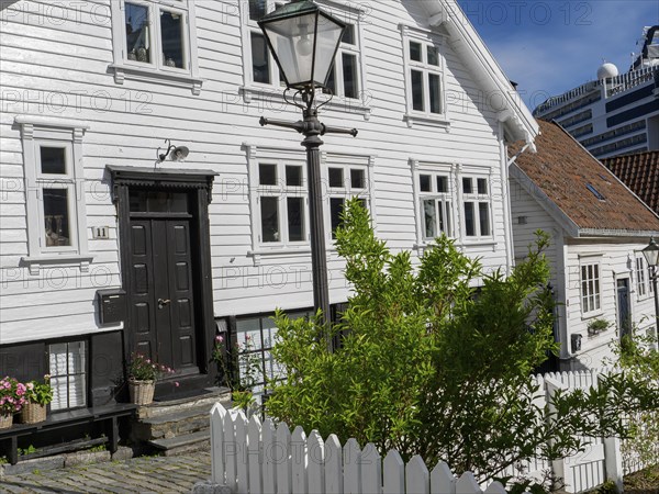 White wooden houses with flowers and black doors along a cobblestone street with a street lamp,