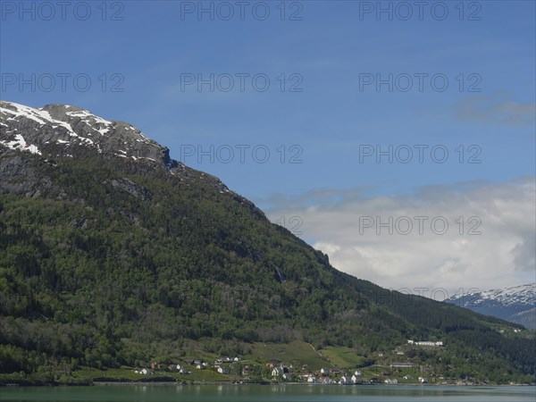 Small settlement in front of a green mountainside and snow-capped peaks under a clear sky, greenish