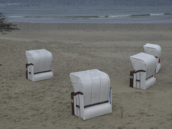 Four white beach chairs on an empty beach with calm sea in the background, beach chairs and beach