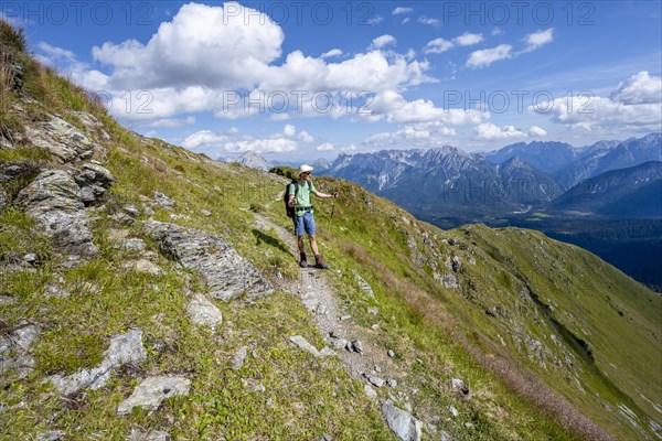 Mountaineer on a hiking trail on a grassy mountain slope, idyllic mountain landscape with green